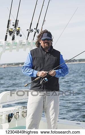 Stock Photograph - Fisherman holding a fishing rod on a boat with a view of the coastline; Cape Cod, Massachusetts, United States of America. Fotosearch