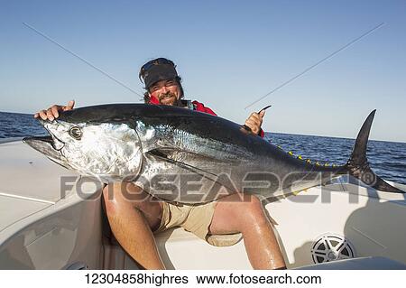 Stock Photograph - Fisherman holds a large fresh fish caught from a boat on the Atlantic ocean; Cape Cod, Massachusetts, United States of America. Fotosearch