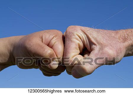 Stock Photograph - Fists pound against each other on a blue background; Spain. Fotosearch