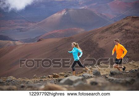 Stock Photograph - Fitness sport couple jogging outside, training together outdoors. Running on amazing trail at sunset, Dramatic beautiful volcano landscape. Fotosearch