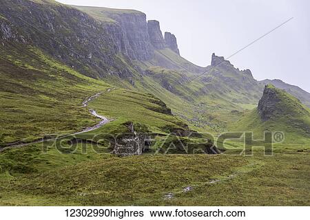 Stock Photograph - Fog covers the green landscape with cliffs and peaks; Scotland. Fotosearch