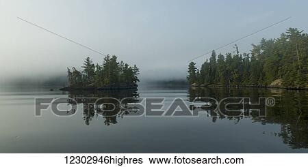 Fog over a tranquil Lake of the Woods and trees reflected along the shoreline; Ontario, Canada View Large Photo Image Stock Photograph - Fog over a tranquil Lake of the Woods and trees reflected along the shoreline; Ontario, Canada. Fotosearch