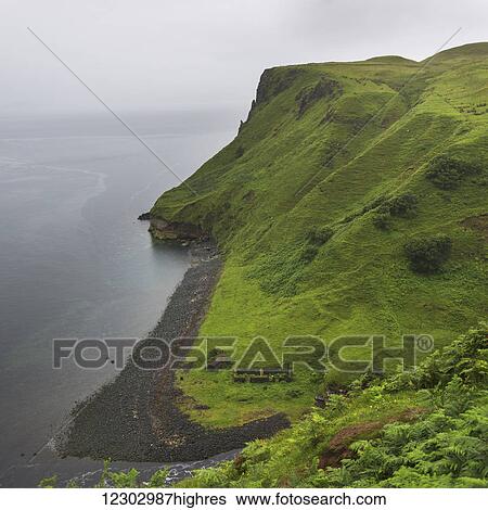 Stock Photograph - Fog over the ocean and lush foliage covered slopes along the coast, Lealt Falls Canyon; Portree, Scotland. Fotosearch
