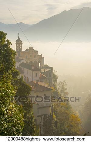 Stock Photograph - Fog sets in over a church and alpine lake; Locarno, Ticino, Switzerland. Fotosearch