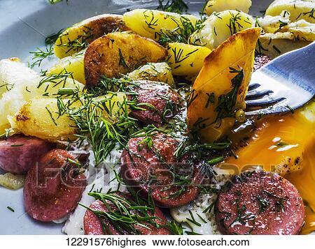 Stock Photograph - Fried eggs with fried potatoes and sausages on plate on old weathered painted table; Kiev, Ukraine. Fotosearch