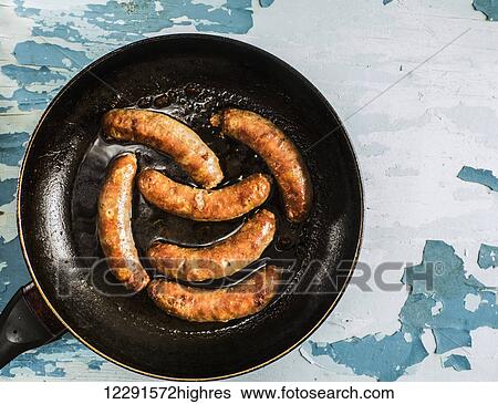 Stock Photograph - Fried homemade sausages in pan on old weathering painted table; Kiev, Ukraine. Fotosearch