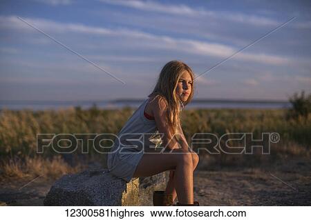 Stock Photograph - Girl in contemplation sitting on a rock on the beach at sunset; Surrey, British Columbia, Canada. Fotosearch