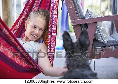 Stock Photograph - Girl relaxing in a hammock and petting her dog; Langley, British Columbia, Canada. Fotosearch