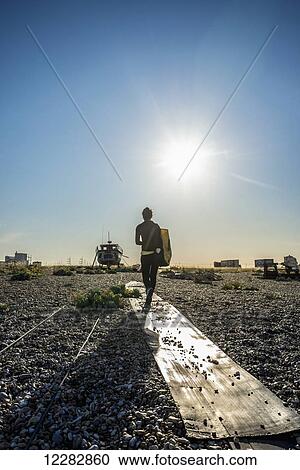 Stock Image - Girl walking on Dungeness shingle beach; Dungeness, Kent, England. Fotosearch