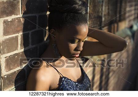 Stock Photograph - Glamorous portrait of a young woman leaning against a brick wall; Toronto, Ontario, Canada. Fotosearch