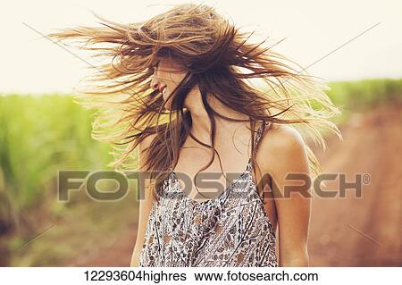 Stock Photograph - Gorgeous Romantic Girl Outdoors. Beautiful Model in Short Dress in Field. Long Hair Blowing in the Wind. Backlit, Warm Color Tones. Fotosearch