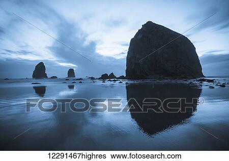 Stock Photograph - Greyish blue colors of dusk behind Haystack Rock; Cannon Beach, Oregon, United States of America. Fotosearch