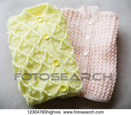 Stock Photograph - Handmade knit baby sweaters in pink and yellow on a grey background. Fotosearch