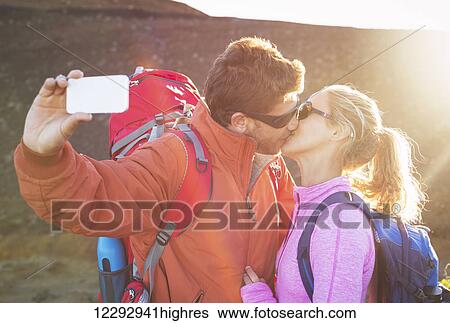 Stock Photograph - Happy couple taking photo of themselves with smart phone outdoors, Taking a selfie. Fotosearch