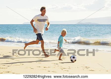 Stock Photograph - Happy Father and Son Having Fun Playing Soccer on the Beach. Fotosearch