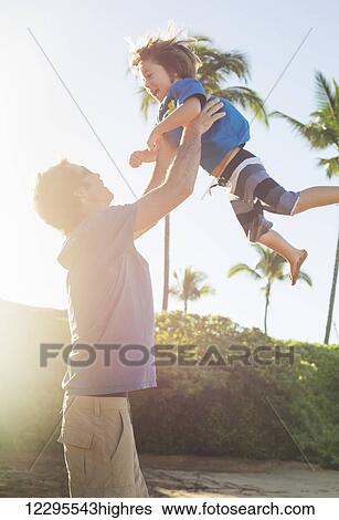Happy father and son playing on tropical beach, carefree happy fun smiling lifestyle View Large Photo Image Stock Photograph - Happy father and son playing on tropical beach, carefree happy fun smiling lifestyle. Fotosearch