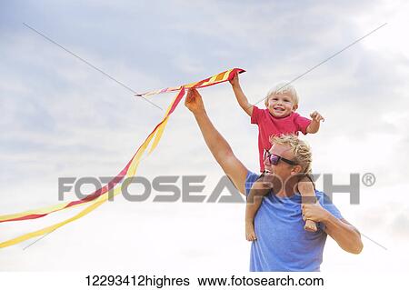 Stock Photograph - Happy father and son playing with kite at the beach at sunset. Fotosearch