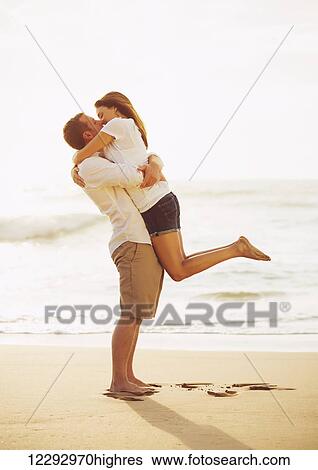 Stock Photograph - Happy Romantic Couple Kissing on the Beach at Sunset. Fotosearch