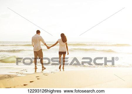 Stock Photograph - Happy Romantic Couple Walking on the Beach Enjoying the Sunset. Fotosearch
