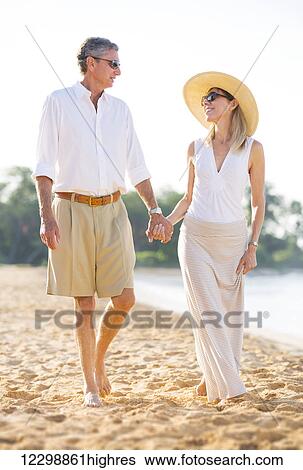 Stock Photograph - Happy Romantic Middle Aged Couple Enjoying Walk on the Beach, Vacation Retirement Concept. Fotosearch