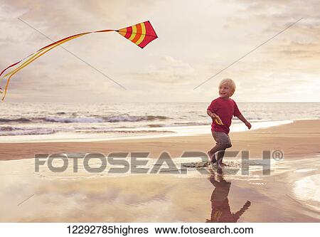Happy young boy flying kite on the beach at sunset View Large Photo Image Stock Photograph - Happy young boy flying kite on the beach at sunset. Fotosearch