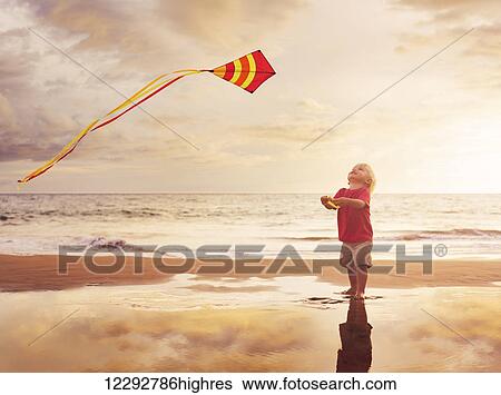 Stock Photograph - Happy young boy flying kite on the beach at sunset. Fotosearch