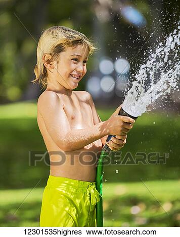 Happy young boy plays with water hose outdoors in yard during summer to cool off in hot weather View Large Photo Image Stock Photograph - Happy young boy plays with water hose outdoors in yard during summer to cool off in hot weather. Fotosearch