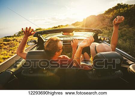 Stock Photograph - Happy Young Carefree Couple Driving Along Country Road in Convertible at Sunset. Fotosearch