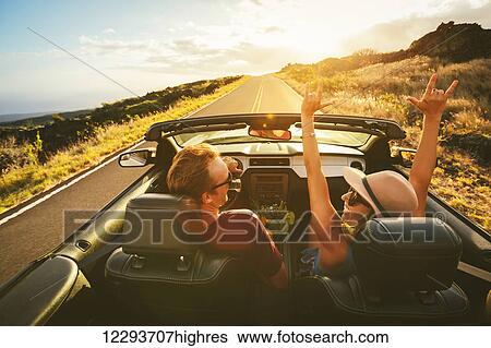 Stock Photograph - Happy Young Carefree Couple Driving Along Country Road in Convertible at Sunset. Fotosearch