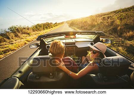 Stock Photograph - Happy Young Couple Driving Along Country Road in Convertible at Sunset. Fotosearch