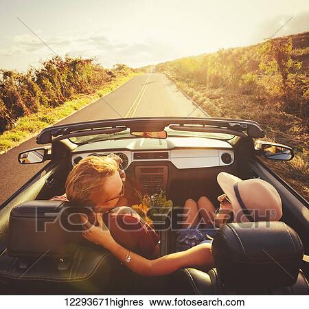Stock Photograph - Happy Young Couple Driving Along Country Road in Convertible at Sunset. Fotosearch