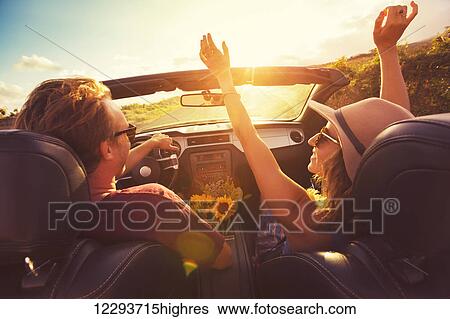 Stock Photograph - Happy Young Couple Driving Along Country Road in Convertable at Sunset. Freedom Adevnture Roadtrip!. Fotosearch