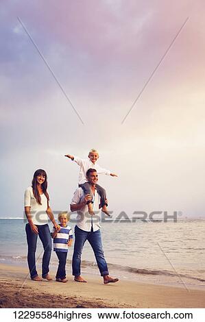Stock Photograph - Happy young family having fun walking on the beach at sunset. Fotosearch