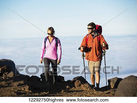Stock Photograph - Hiking in the mountains. Happy athletic couple with backpacks enjoying hike outdoors on beautiful mountain trail.. Fotosearch