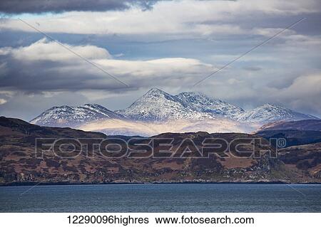 Hills along the coastline and peaked snow covered mountains under a cloudy sky; Argyll, Scotland View Large Photo Image Stock Photograph - Hills along the coastline and peaked snow covered mountains under a cloudy sky; Argyll, Scotland. Fotosearch