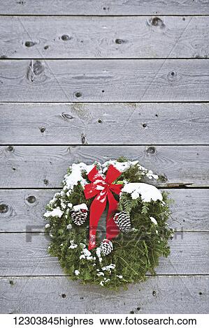 Stock Photograph - Holiday wreath hanging on the side of a wooden shed after a dusting of snow; Homer, Alaska, United States of America. Fotosearch