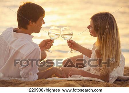 Honeymoon concept, Man and Woman in love, Couple enjoying glass of champagne on tropical beach at sunset, Beautiful sunset light View Large Photo Image Stock Photograph - Honeymoon concept, Man and Woman in love, Couple enjoying glass of champagne on tropical beach at sunset, Beautiful sunset light. Fotosearch