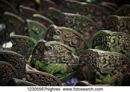 Stock Photograph - In a factory that produces terra-cotta statues for gardens, the broken or flawed ones are discarded, soon becoming swallowed up by the jungle. These are temple lions; Chiang Mai, Thailand. Fotosearch