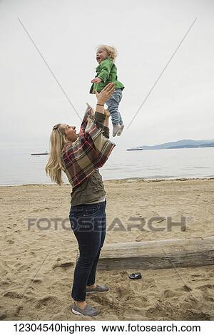 In a winter beach scene, a mother joyfully throws her little girl in the air; Vancouver, British Columbia, Canada View Large Photo Image Stock Photograph - In a winter beach scene, a mother joyfully throws her little girl in the air; Vancouver, British Columbia, Canada. Fotosearch