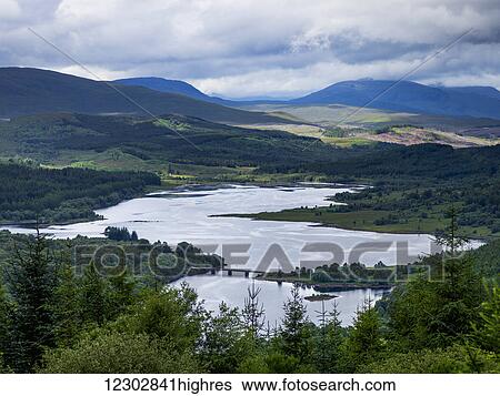 Stock Photograph - Landscape of a river and forests over mountains under a cloudy sky; Scotland. Fotosearch