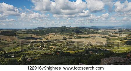 Stock Photograph - Landscape of rolling hills under a blue sky with cloud; Montepulciano, Umbria, Italy. Fotosearch