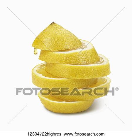 Stock Photograph - Lemon slices piled on a white background with a droplet of liquid falling from the rind; Toronto, Ontario, Canada. Fotosearch
