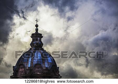 Stock Photograph - Light breaks through the turbulent clouds on the dome of the Santi Luca e Martina church; Rome, Italy. Fotosearch