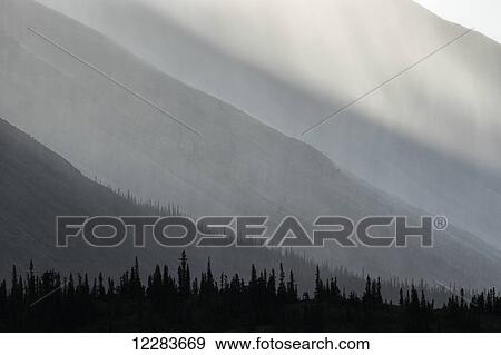 Light shines through the rain as it falls on the mountains along the Wind River in the Peel Watershed; Yukon, Canada View Large Photo Image Stock Photo - Light shines through the rain as it falls on the mountains along the Wind River in the Peel Watershed; Yukon, Canada. Fotosearch