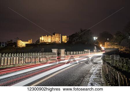 Stock Photograph - Light trails on a road and illuminated building in the background at nighttime; Alnwick, Northumberland, England. Fotosearch