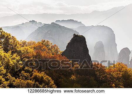 Stock Photograph - Low cloud around the rugged cliffs with foliage in autumn colours; Meteora, Greece. Fotosearch