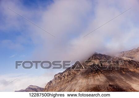 Stock Photograph - Low clouds hang at the top of of eroding red cliffs in the Brooks Range; Alaska, United States of America. Fotosearch
