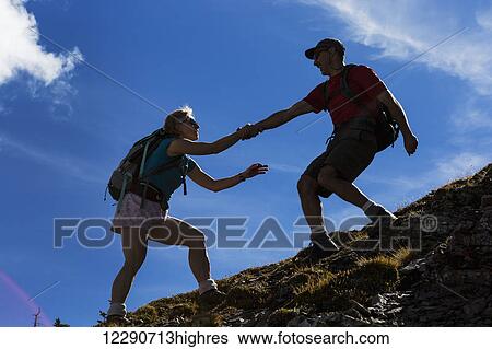 Male hiker helping female hiker up a rocky slope with blue sky and clouds; Waterton, Alberta, Canada View Large Photo Image Stock Photograph - Male hiker helping female hiker up a rocky slope with blue sky and clouds; Waterton, Alberta, Canada. Fotosearch