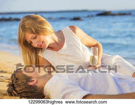 Man and Woman in love, Couple enjoying glass of champagne on tropical beach at sunset, Honeymoon concept View Large Photo Image Stock Photograph - Man and Woman in love, Couple enjoying glass of champagne on tropical beach at sunset, Honeymoon concept. Fotosearch