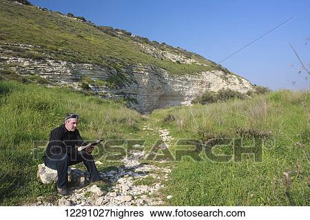 Stock Photograph - Man sitting on a rock and reading his Bible in the Valley of Elah; Israel. Fotosearch